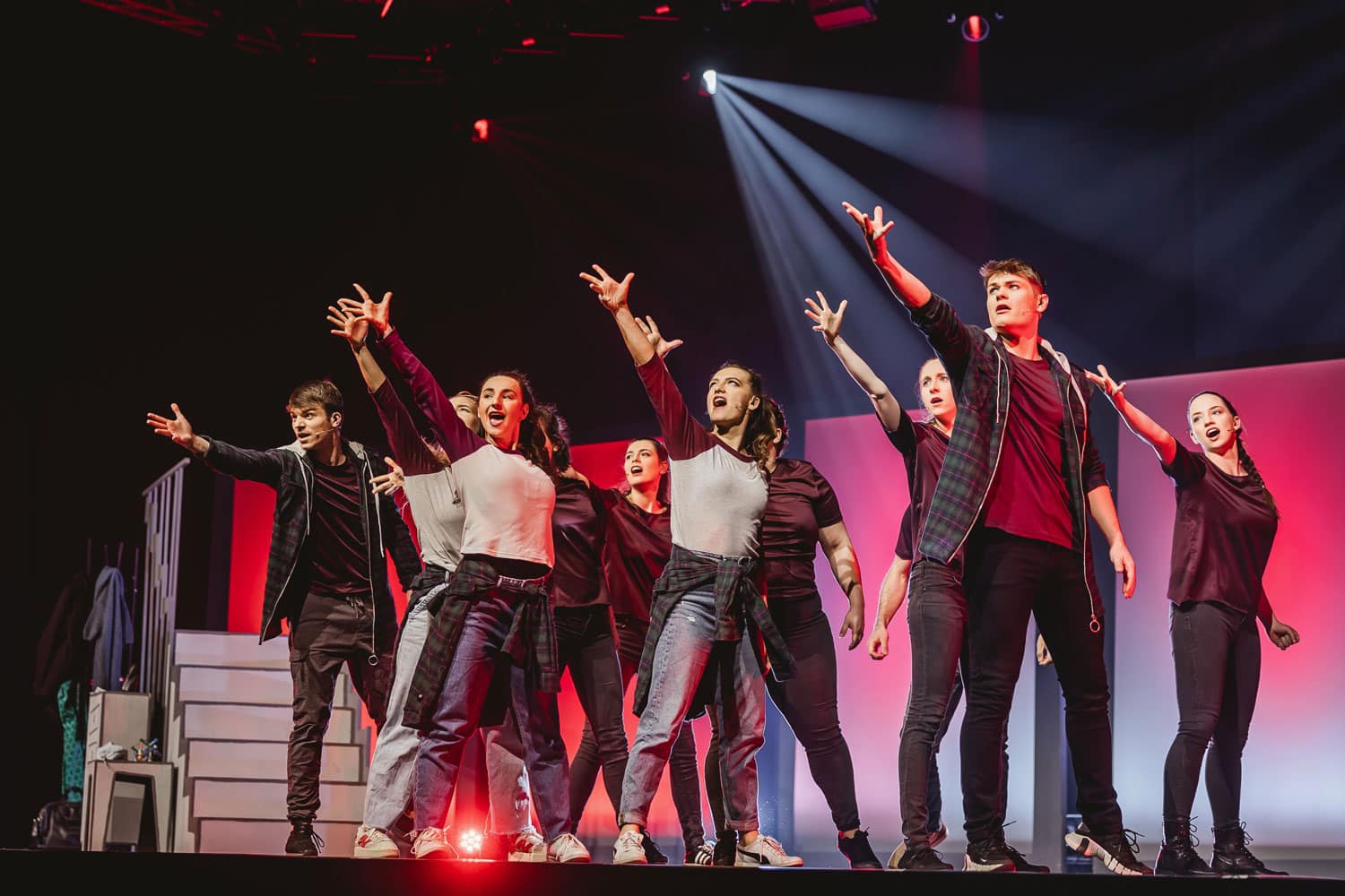Schauspieler stehen singend auf der Bühne und strecken den einen Arm nach oben.